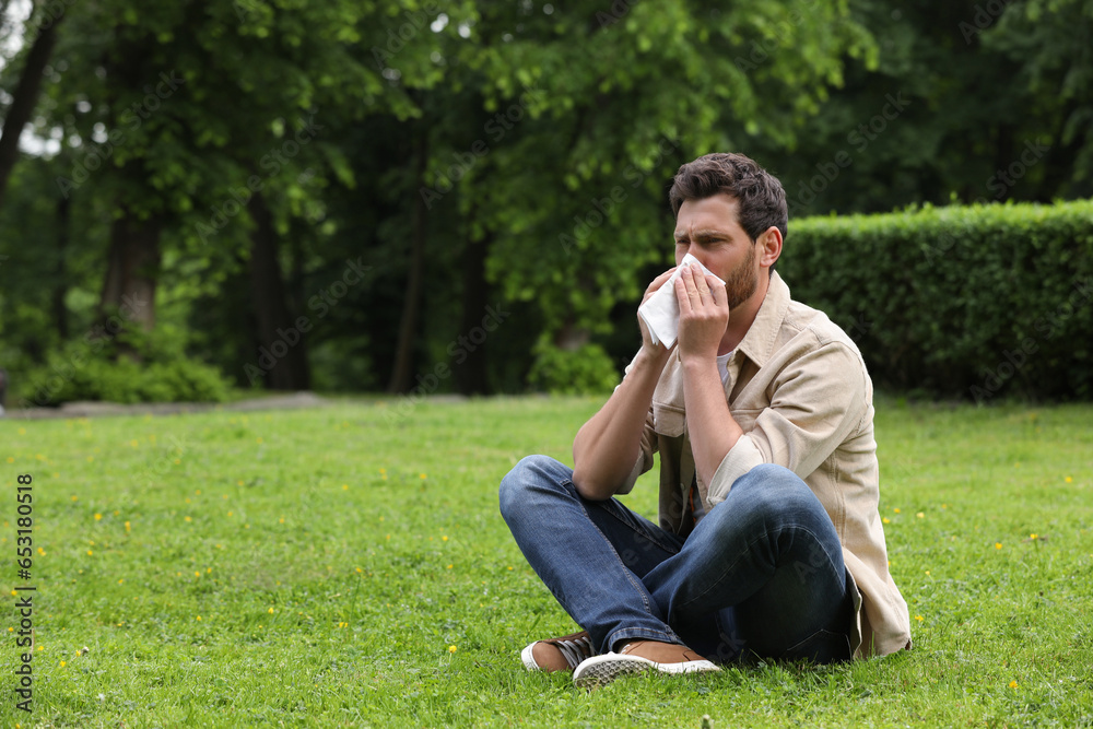 Man suffering from seasonal spring allergy on green grass in park. Space for text Man suffering from seasonal spring allergy on green grass in park. Space for text