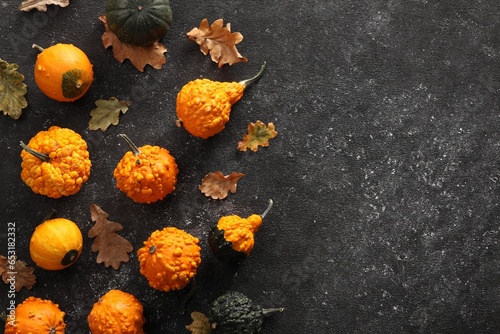 Different fresh ripe pumpkins and dry leaves on black textured table, flat lay. Space for text