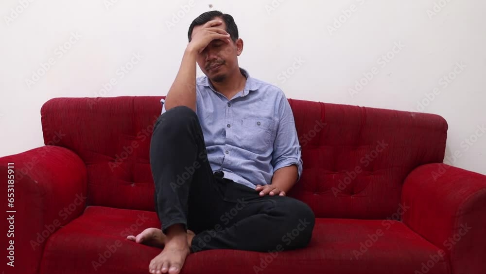Worried asian middle-age man in deep thinking while sitting on sofa at home. Concept of financial problem, love breakup and mental illness Worried asian middle-age man in deep thinking while sitting on sofa at home. Concept of financial problem, love breakup and mental illness