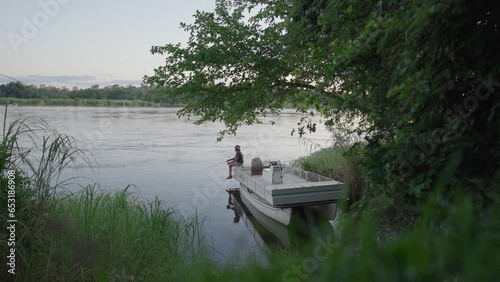 Man fishing off a parked boa on the edge of the flowing Zambezi river photo