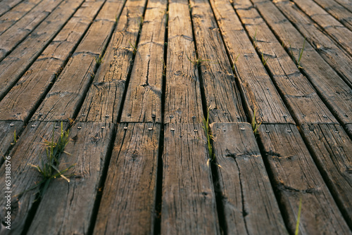 Exterior wooden deck with a texture very marked by the passage of time and aged with grass sprouts between the planks