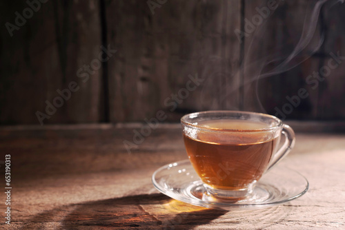 hot tea into a teacup. A cup of herbal tea placed on an old wooden table, dark background. A day with light sunlight Shining on the warm atmosphere in winter
