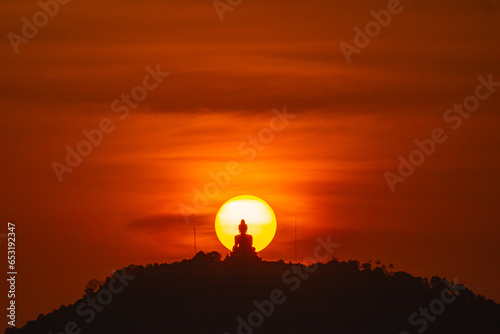 Fototapeta Naklejka Na Ścianę i Meble -  Stunning red sky sunset the round sun is on the back of Phuket big Buddha on the high mountain. .landmark of Phuket island..Phuket big Buddha in circle of the sun in red sky..red sky background.