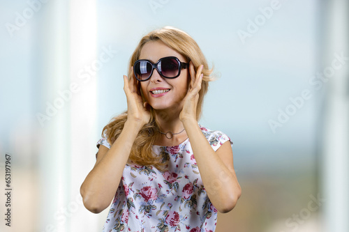 Smiling blonde woman wearing sunglasses indoors. Portrait of caucasian middle aged against window background. photo