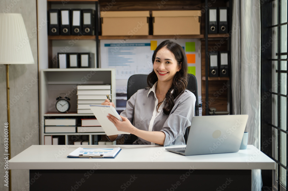 Confident beautiful Asian businesswoman typing laptop computer and digital tablet while holding tablete at office Confident beautiful Asian businesswoman typing laptop computer and digital tablet while holding tablete at office