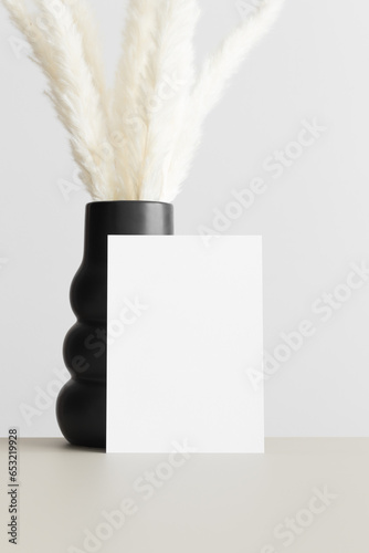 White invitation card mockup with a pampas decoration on the beige table. 5x7 ratio, similar to A6, A5.