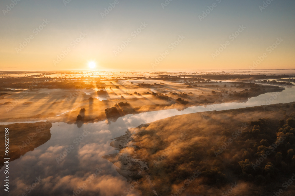 Morning sunrise on the big river. The photo was taken from a drone, there is beautiful fog and a blue winding river below.  View of a field next to a river.