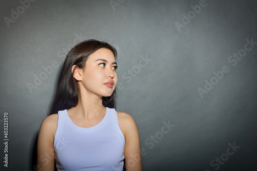 Close-up portrait of a young Asian woman with light makeup and smooth beautiful skin, turned her head to the side. Young pretty girl in a white T-shirt looks away with interest