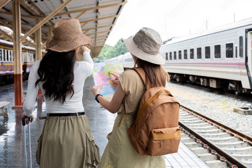 Two women look at tourist maps while waiting to travel at the train station.