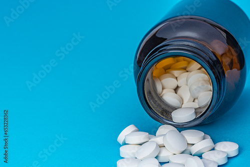 White round pills scattered from a brown bottle on a blue background. Pharmacy and healthcare theme. 