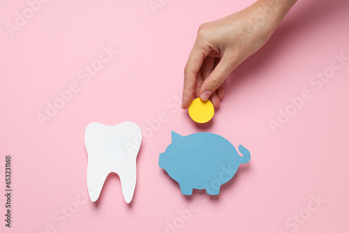 Paper tooth, piggy bank and coin in hand on pink background, top view