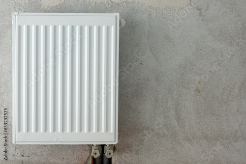 A white new metal hot water heating radiator is attached to a raw gray wall. Background. Form.