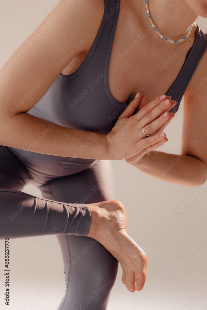 Attractive woman bending body close up. Athletic woman stretches her body on a mat in the studio. A strong muscular sportswoman is engaged in gymnastics on a light background