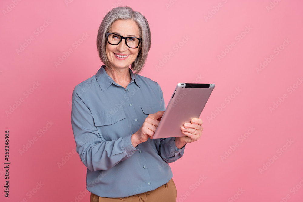 Portrait of pleasant nice person with gray short hair wear stylish shirt arms hold tablet typing message isolated on pink background Portrait of pleasant nice person with gray short hair wear stylish shirt arms hold tablet typing message isolated on pink background