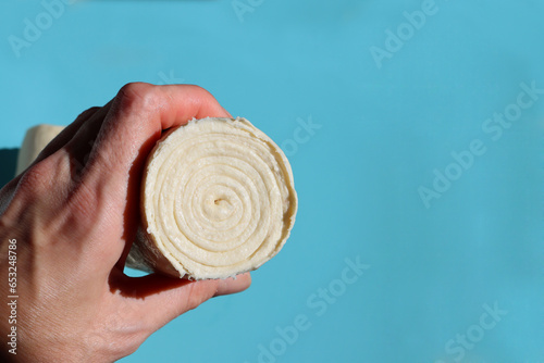 Woman's hand holding a roll of dough on a blue background.