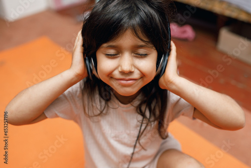 Spanish girl with dark hair listens to music on headphones inside the house, orange background, close-up photo