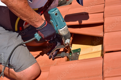 Dachdecker beim Aufbau einer Photovoltaikanlage auf einem neu gedeckten Ziegeldach: Justage und Verschraubung der Halterungen und Klemmen für das Schienensystem an den Dachsparren photo