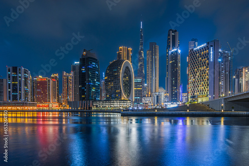 Skyline of Dubai in the evening at the blue hour. illuminated office and commercial buildings from the financial center of the city in the united arab emirates. Reflection on the smooth water surface