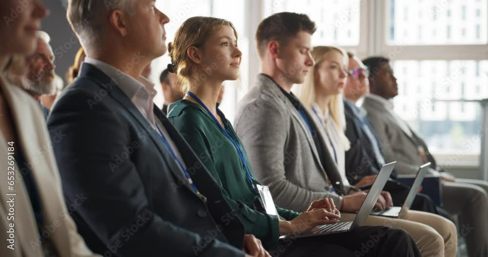Young Woman Sitting in Crowded Audience at a Business Conference. Female Delegate Smiling and Using Laptop Computer. Manager Watching Motivational Presentation About Investing In Innovative Startups.