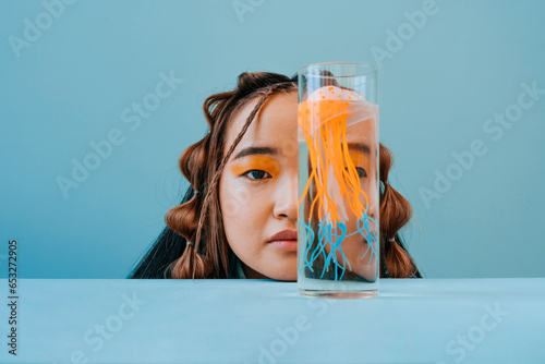 Young woman covering half face with jellyfish in glass photo