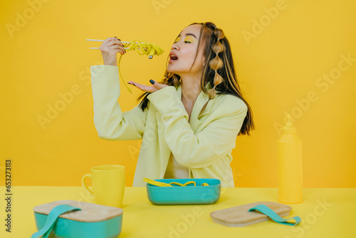 Young woman having wired noodles against yellow background