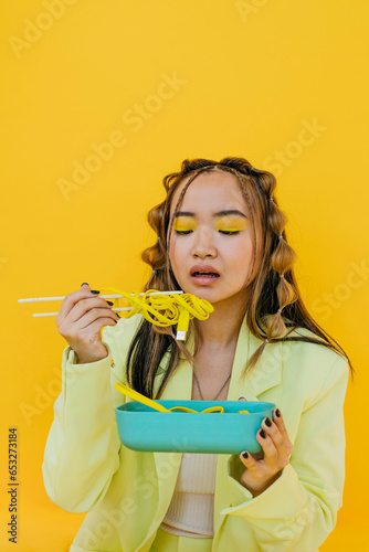 Young woman eating noodles like wire from bento box against yellow background photo