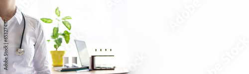 Doctor woman in her office. Doctor with stethoscope on the blured background of her office table with lap top, laboratory dishes, notepads, books and potted flower. Health care concept. Long banner.