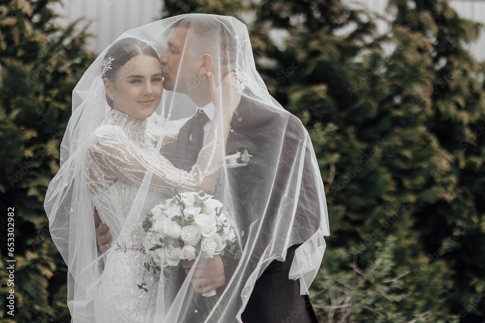 The bride in an elegant dress with a bouquet and the groom in a classic suit are walking in the garden, holding hands. The bride in an elegant dress with a bouquet and the groom in a classic suit are walking in the garden, holding hands.