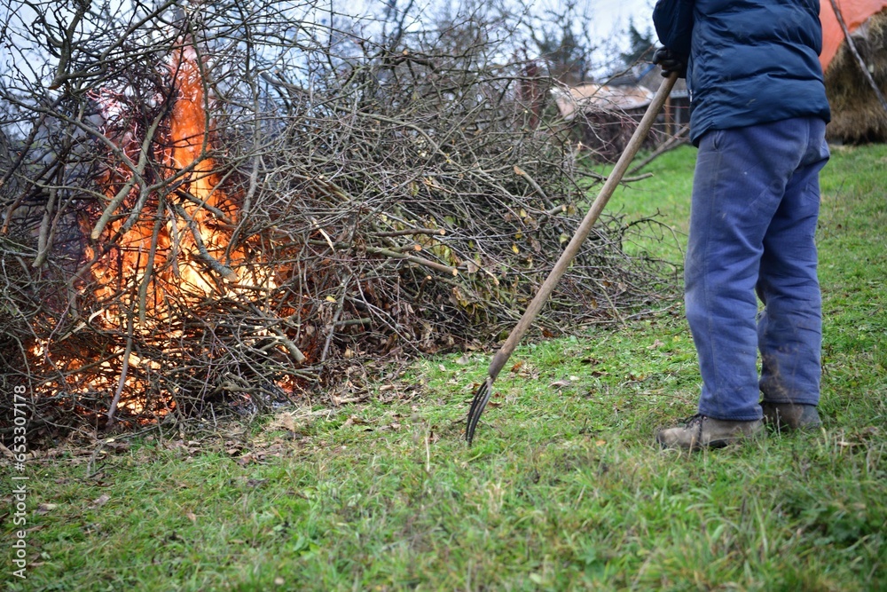 A gardener burns waste branches in a garden in a village traditionally