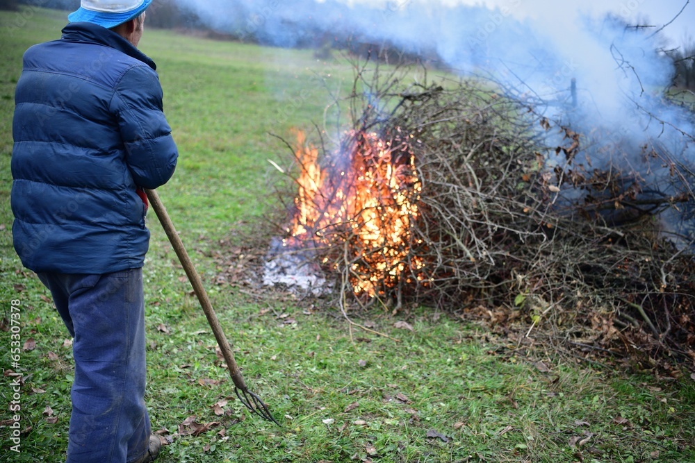 A gardener burns waste branches in a garden in a village traditionally