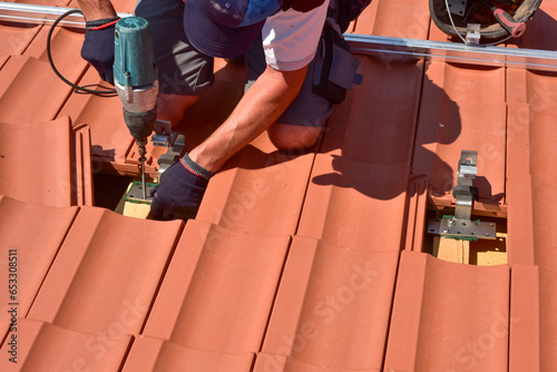 Dachdecker beim Aufbau einer Photovoltaikanlage auf einem neu gedeckten Ziegeldach: Justage und Verschraubung der Halterungen und Klemmen für das Schienensystem an den Dachsparren photo