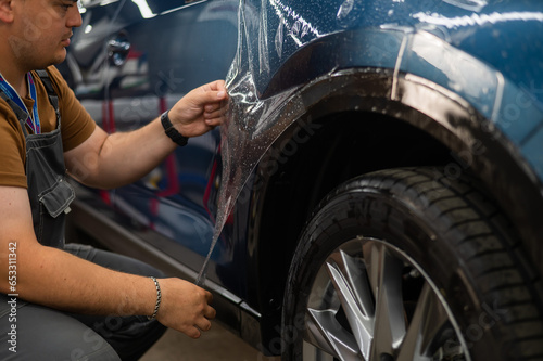 The master in the car service applies a protective armor film to the car body. 