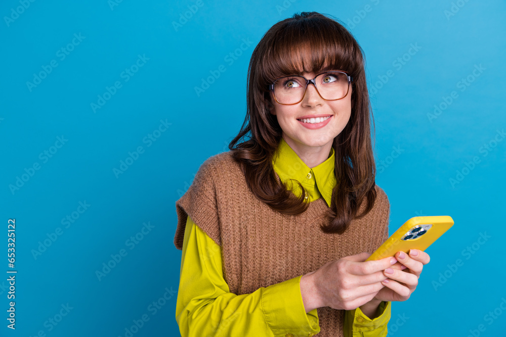 Photo of positive dreamy lady wear brown vest spectacles typing modern gadget looking empty space isolated blue color background Photo of positive dreamy lady wear brown vest spectacles typing modern gadget looking empty space isolated blue color background