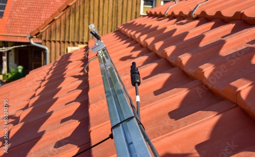Dachdecker beim Aufbau einer Photovoltaikanlage auf einem neu gedeckten Ziegeldach: Befestigung der Steckverbinder für die Solarmodule