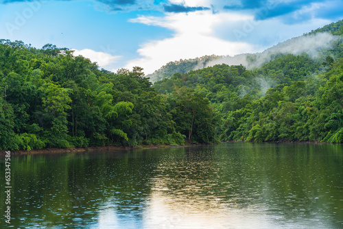 A small lake in Thailand surrounded by mountains with lush green forest and mist.