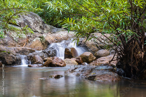 A small waterfall with many rocks in the stream. Surrounded by trees in the mountain forest.