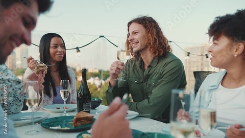 Funny multinational friends celebrate holiday and eating at open air table in restaurant