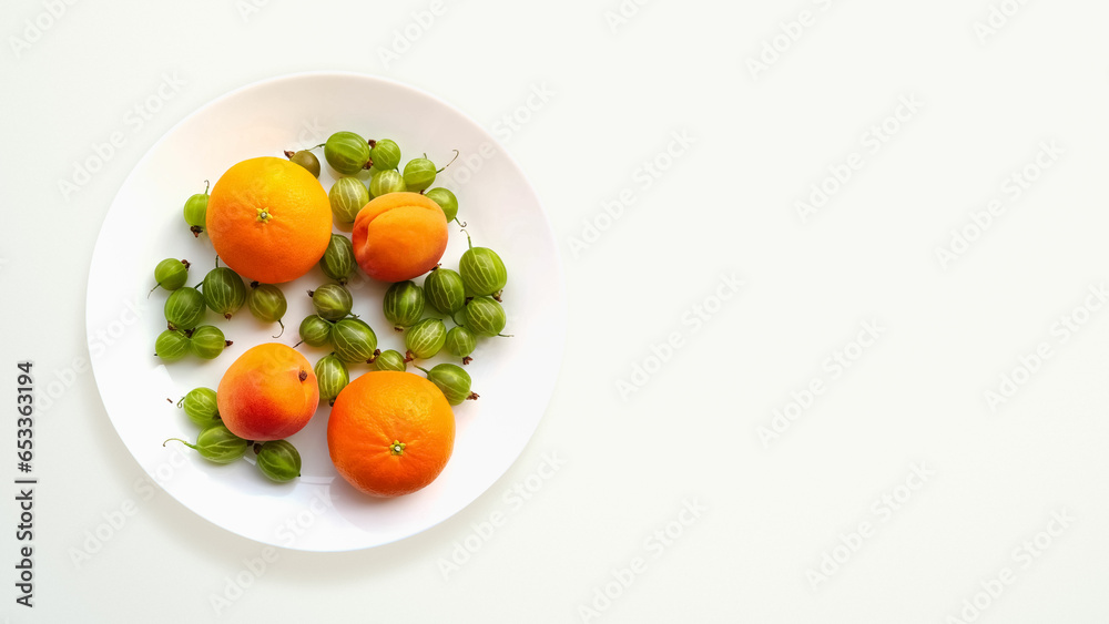 A plate with bright fruits and berries: oranges, apricots and gooseberries. White background with copy space.