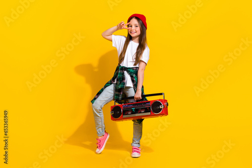 Full body photo of cute small girl showing v-sign hold tape recorder wear trendy white clothes isolated on yellow color background