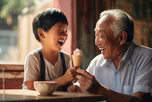 Cheerful Asian grandfather and grandchild eating ice cream outdoors on sunny summer day. Granddad sharing a dessert with a child in outdoor cafe.