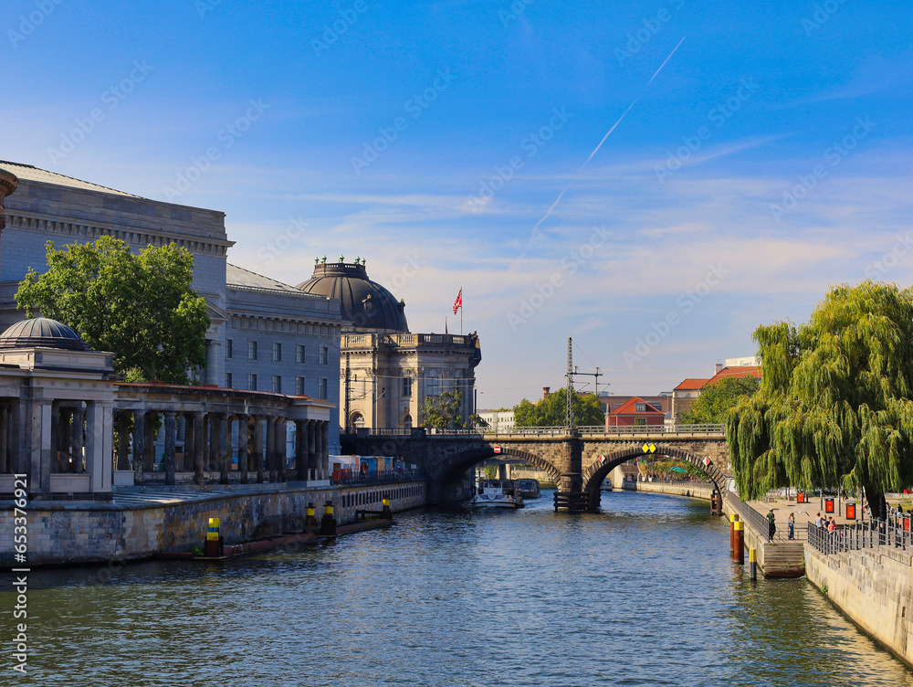 Fototapeta premium Blick über die Spree auf die Kolonnaden der Museumsinsel und die Friedrichsbrücke am James-Simon-Park unter blauem Himmel, Berlin, Deutschland
