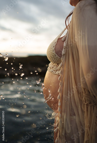 Pregnant woman in profile close-up in water splashed with drops