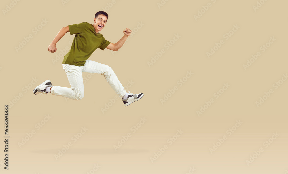 Energetic teenage boy joyfully running and jumping in hurry to catch crazy discounts. Stylish guy running near copy space, isolated on beige background. Concept of discounts on goods for teenagers.