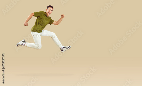 Energetic teenage boy joyfully running and jumping in hurry to catch crazy discounts. Stylish guy running near copy space, isolated on beige background. Concept of discounts on goods for teenagers.
