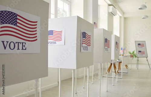 Interior of an empty polling place in the US. Row of empty white voting booths with American flags at the ballot station. Elections in the USA, democracy concept 