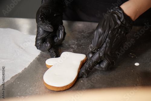the cook holds a ready made cookie covered with white icing with his gloved hands