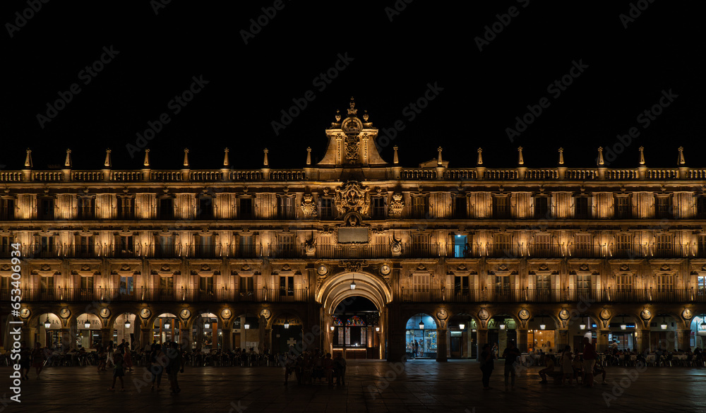 Plaza Mayor of Salamanca, at night, with all the lights illuminating the façade and the Salamanca City Hall. Tourists walking and dining and drinking on the terraces of bars and restaurants