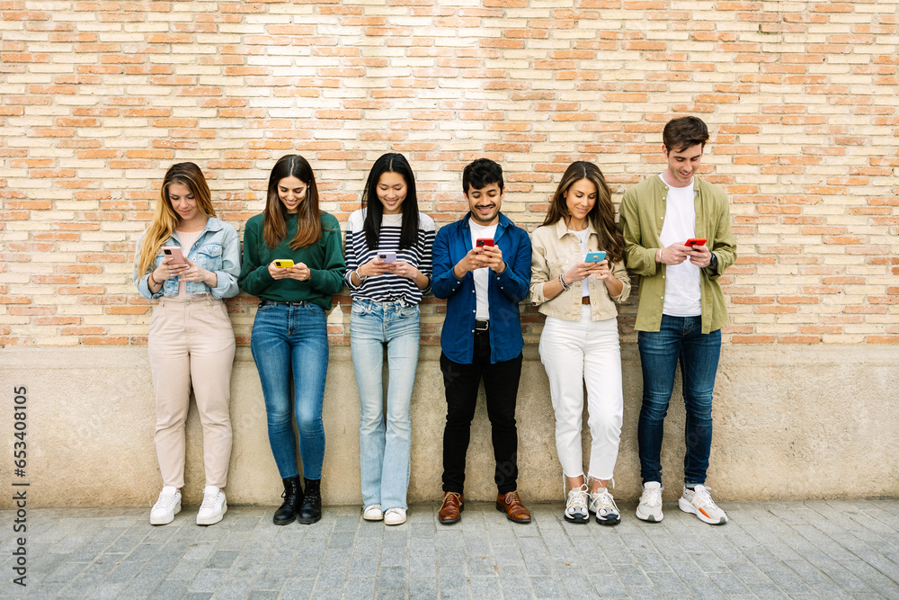 © Xavier Lorenzo - Happy group of young people using mobile phone device leaning together over wall background. Millennial friends generation laughing and having fun connected at social media network on smartphone.