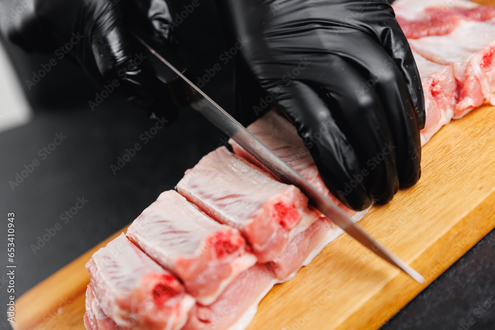 Butcher woman with knife cuts fresh meat pork ribs with on wooden board on dark background