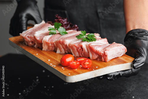 Butcher woman hold wooden board with fresh meat pork ribs on dark background